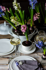 Beautiful elegant table setting for Easter celebration with fresh spring hyacinth flowers, burning candles. Romantic wedding dinner table decoration. Springtime, home gardening. Dark background
