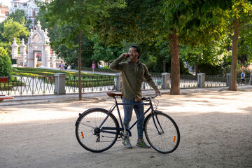 Young man talking on phone with bicycle in park