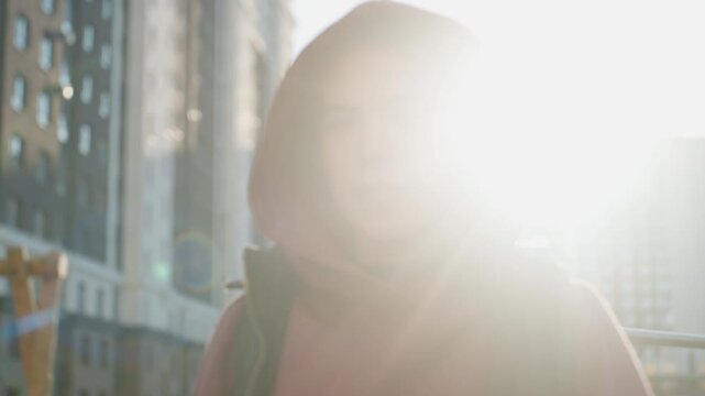 Portrait of young fair athlete smiling under sunny sky in urban park setting with confident calm expression and relaxed posture, hoodie vest combo and sunlit highlights in vibrant city scene