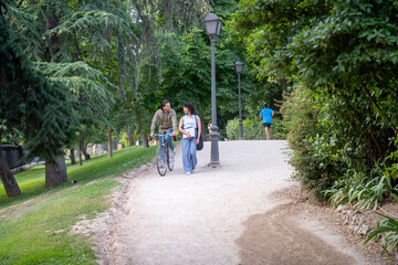 Obraz premium Interracial couple walking bicycle in green park