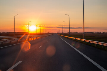 Obraz premium A view of a highway at dusk at sunset. A smooth strip of highway devoid of traffic