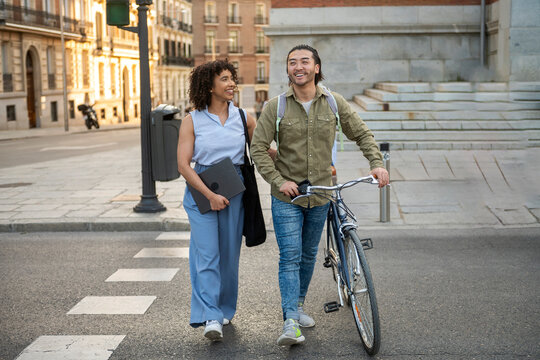 Interracial couple walking across city crosswalk pushing bicycle - Powered by Adobe