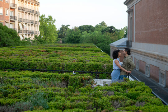 Interracial couple embracing on green hedge garden balcony - Powered by Adobe