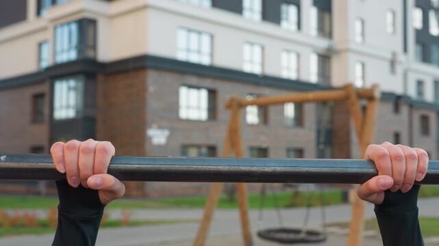 Hand view of energetic trainer exhaling while gripping horizontal pull up bar in urban park gym with autumn foliage backdrop showcasing forearm strength focus and control during calisthenics