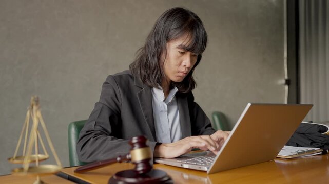 Female lawyer in suit working digitally on laptop at law office desk, showing modern legal practice.