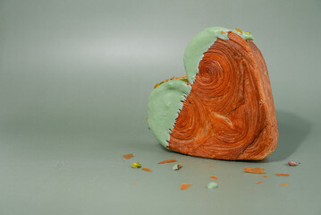 Heart shaped pistachio croissant on green background with copy space. Puff pastry new trendy sweet dessert bakery. Creamy dough experiment 