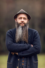 Bearded man in traditional wool jacket and hat outdoors, portrait of rural lifestyle