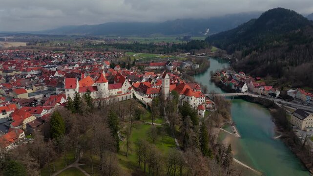 Fuessen medieval gem in Bavaria, features striking Hohes Schloss atop hill, St. Mang Church and charming cobblestone streets. Spring colors and scenic mountain views make perfect travel destination. 