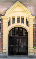 black wooden door with arched yellow facade and small upper windows, classic european architecture detail, symmetrical entrance front view
