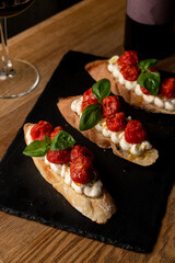 Freshly baked slices of bread hold creamy cheese and vibrant sun-dried tomatoes, garnished with fragrant basil leaves on a dark slate plate, perfect for a casual dinner