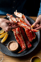 Hands expertly crack open fresh crab legs, revealing tender meat, while vibrant lemon wedges and savory sauces accompany this delightful seafood experience in a warm atmosphere