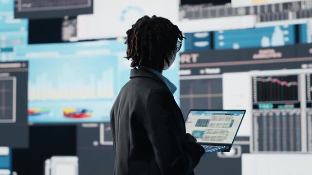 Manager using laptop software to compare company metrics on digital videowall before making decisions. Entrepreneur analyzing key performance indicators using notebook program, camera B