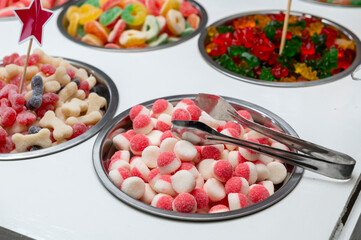 Snack bar cart with colorful and flavored candies and sweets, marshmallows, and fruit jellies for parties and events to serve in small cups.
