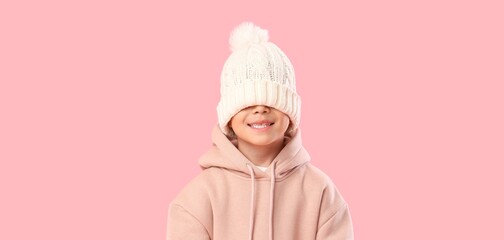 Funny little boy in white knitted hat on pink background