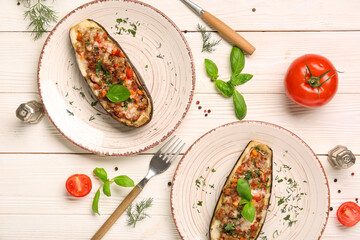 Plates with stuffed eggplants, tomatoes, dill and basil leaves on white wooden background