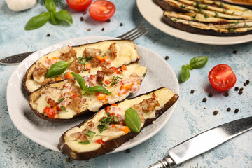 Plate with stuffed eggplants, tomatoes, peppercorns and basil leaves on blue grunge background