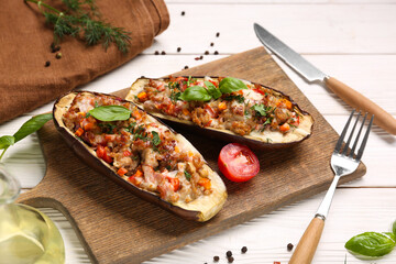 Board with stuffed eggplants, peppercorns and basil leaves on white wooden background