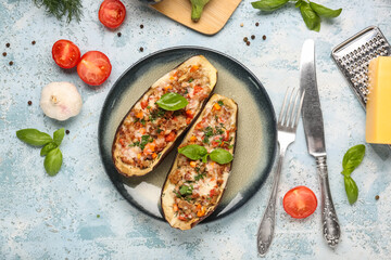 Plate with stuffed eggplants, tomatoes, garlic and basil leaves on blue grunge background