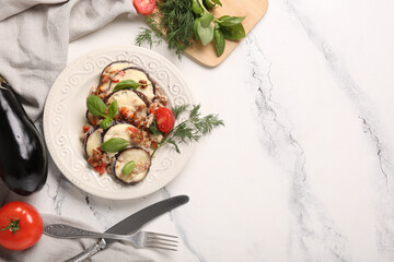 Plate with baked eggplant slices, tomato, dill and basil leaves on marble background