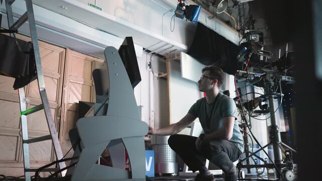 Man crouching in professional studio, adjusting digital monitor and timer settings on equipment, focused on work in high-tech filming environment, production process in progress