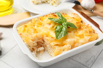 Baking dish of pasta with basil leaves and cheese on white tile background