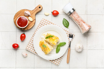 Plate with portion of baked pasta, tomatoes, garlic and basil leaves on white tile background