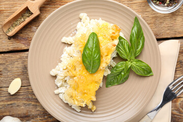 Plate with portion of baked pasta, garlic and basil leaves on wooden background