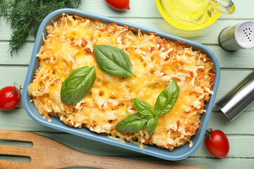 Baking dish of pasta with basil leaves, tomatoes and dill on green wooden background