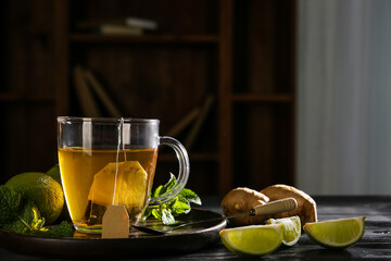 Cup of hot tea with limes, mint leaves and ginger on wooden table against dark background