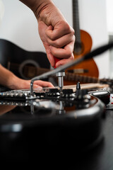 Technician fine-tunes the chrome bridge of a black electric guitar with a screwdriver. Chrome bridge of the electric guitar is tightened with a screwdriver. Adjusting Guitar Bridge with Screwdriver.