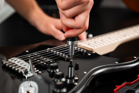 Adjusting Guitar Bridge with Screwdriver. Technician fine-tunes the chrome bridge of a black electric guitar with a screwdriver. Chrome bridge of the electric guitar is tightened with a screwdriver.