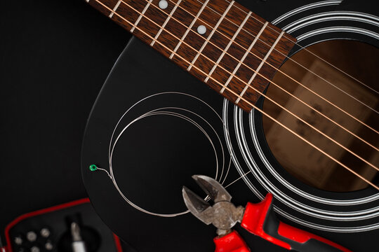 Guitar string replacement with tools. Acoustic guitar setup in progress with new strings and essential tools on the table. Restringing process with pliers and screwdriver kit near acoustic guitar.