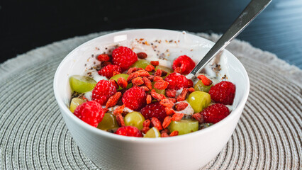 A beautiful and healthy yogurt bowl topped with fresh raspberries, grapes, chia seeds, and vibrant goji berries. A nutritious and colorful breakfast or snack.
