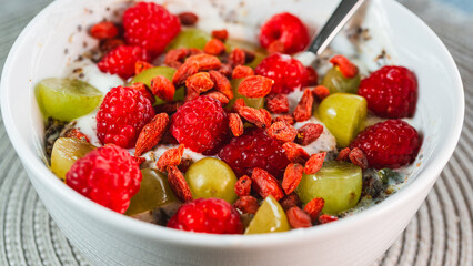 A beautiful and healthy yogurt bowl topped with fresh raspberries, grapes, chia seeds, and vibrant goji berries. A nutritious and colorful breakfast or snack.