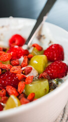 A beautiful and healthy yogurt bowl topped with fresh raspberries, grapes, chia seeds, and vibrant goji berries. A nutritious and colorful breakfast or snack.
