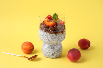 Glass of tasty chia seed pudding with granola and apricots on yellow background