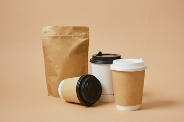 Various cardboard takeaway coffee cups and zip-lock paper bag mock-ups, coffee beans in packaging, beige background