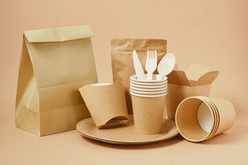 Eco friendly food packagings, tableware, paper bags, cups, wooden forks, spoons and knives beige background