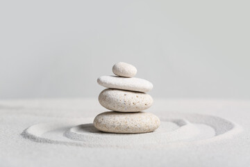 Stack of spa stones on light sand against grey wall. Zen concept