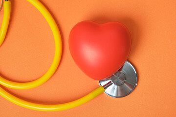 Medical stethoscope and red heart, orange backgroud. Health care and heart check concept.