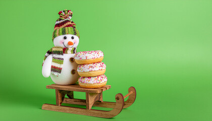Snowman with donuts on wooden sled against green background