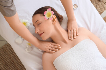Beautiful young happy woman with plumeria flowers getting massage on couch in spa salon, top view