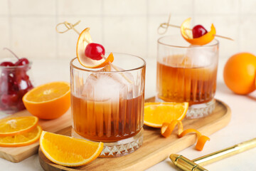 Glasses of tasty Old Fashioned Cocktail with cherries and oranges on light background
