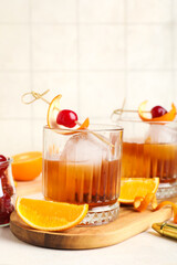 Glasses of tasty Old Fashioned Cocktail with cherries and oranges on light background