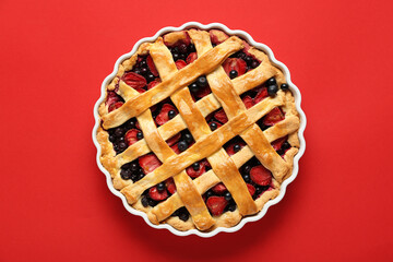 Baking dish with tasty berry pie on red background