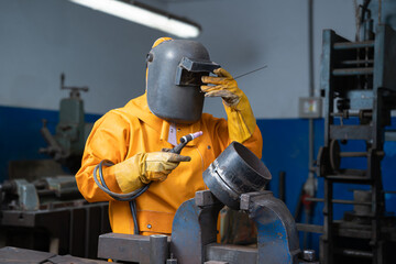 Welder with yellow jacket, hand on helmet.