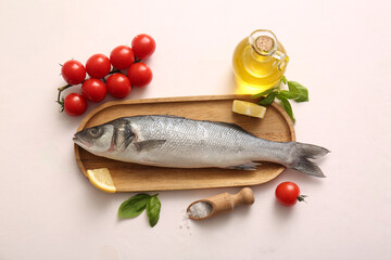 Wooden board with fresh raw seabass fish and different ingredients on white background