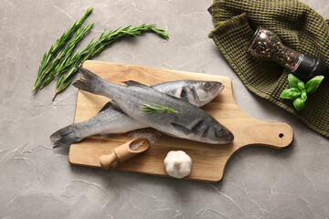 Wooden board with fresh raw seabass fishes and different spices on grey background