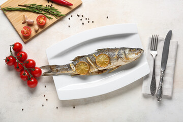 Plate with delicious cooked seabass fish, lemon slices and tomatoes on light background