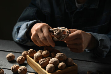 Elderly woman cracking walnuts with nutcracker on black wooden table